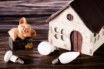 Led lamps and piggy bank lie on a near the house layout wooden background