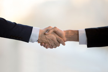 Close up two businessmen in suits shake hands greeting each other. Executive manager and client after successful negotiations handshaking. Boss congratulate new company employee is glad to cooperate