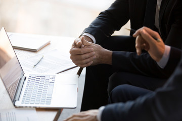 Close up of businessmen in formal suits sitting near table using computer working together at meeting preparing presentation or discussing and analyzing contract agreement details terms and conditions