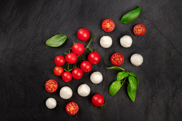 A flat lay composition with Mozzarella cheese, cherry tomatoes and basil leaves on a dark background, Italian cuisine ingredients with a place for text
