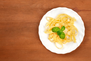 A top-down view of a plate of Italian pasta with Parmesan cheese and fresh basil leaves, shot from the top on a dark rustic wooden background with copy space