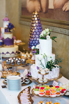 Candy bar table set. Cookies, eclairs, macaroons, fruits, cream and layered cakes. Pastel violet colours.