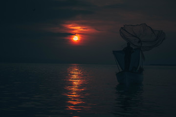 Sun goes down while fisherman throws his fishnet to collect fishes