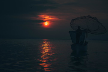 Sun goes down while fisherman throws his fishnet to collect fishes