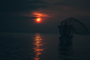Sun goes down while fisherman throws his fishnet to collect fishes