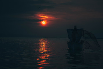 Sun goes down while fisherman throws his fishnet to collect fishes