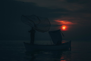 Sun goes down while fisherman throws his fishnet to collect fishes