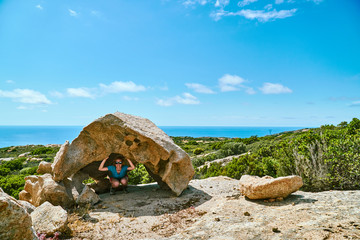 Funny tourist girl under the stone formation in Corsica Corse France above the sea on sunny day