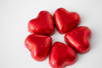 Obraz na płótnie Canvas valentines day, sweets and confectionery concept - close up of red heart shaped chocolate candies on white background