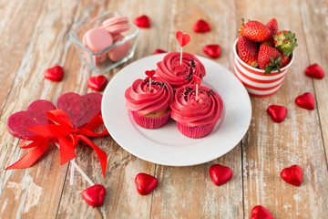 valentines day, sweets and romantic concept - close up of frosted cupcakes, red heart shaped chocolate candies, lollipops and strawberries