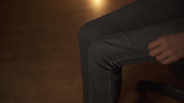 The girl in blue jeans sits in her room in the evening on a chair and wears white socks.