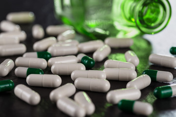 Close-up pile of white color medical pills on background vintage medical bottle made of green glass