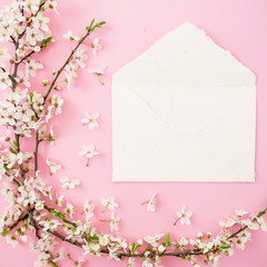 Floral frame with spring tree flowers and white paper vintage envelope on pink background. Flat lay, top view.