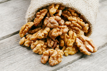 Walnuts in a burlap bag on a wooden gray background.