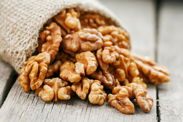 Walnuts in a burlap bag on a wooden gray background.