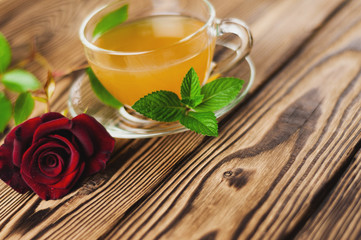 Glass cup with green tea and mint near red rose on sprig on old wooden table. Saint Valentine's Day concept