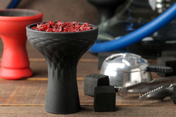 silicone bowl for hookah with tobacco and various accessories for making hookah. coals, tongs, kolaud on a brown wooden table. close-up. accessories for hookah.