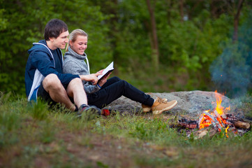 A couple of tourists in time of the hike, sitting and relaxing near the fire embracing,