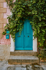 Beautiful teal entrance door to the house surrounded by green foliage plants in Corsica