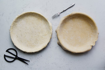 Raw uncooked pie crust in baking pan for two pies on concrete background
