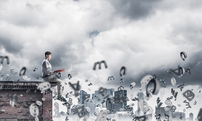 Man on roof edge reading book and symbols flying around