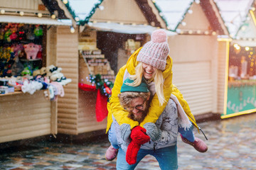 Happy winter travel student couple. Man giving woman piggyback ride on winter vacation in city...