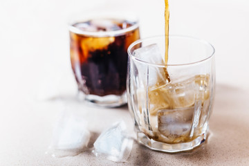 A jet of cola in a glass with ice, bubbles and foam - close-up and copy space