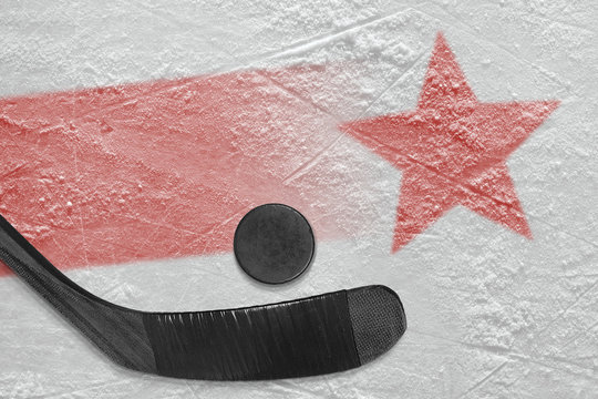 An image of a red line with a red star on ice and a stick with a puck