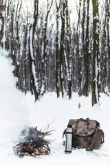 Thermos with hot tea, coffee. Camp fire an in winter time, surrounded by snow forest. Concept adventure active vacations outdoor hiking sport, vertical photo