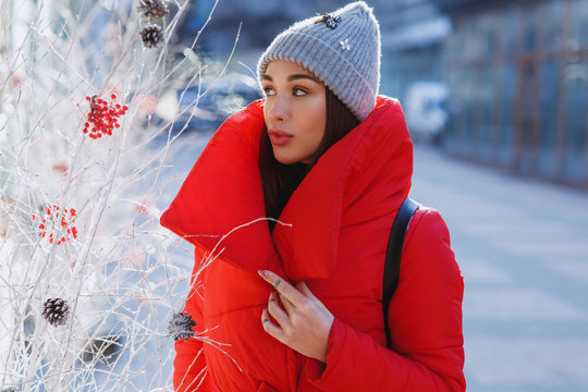 Beautiful woman in red winter jacket walks along the street covered with snow in a beautiful old European city. Christmas, new year and winter holiday concept - Image