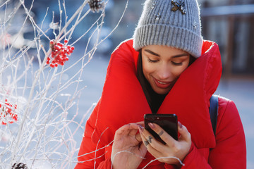 happy woman in red winter down jacket and knitted grey hat types text of sms or message  in her...