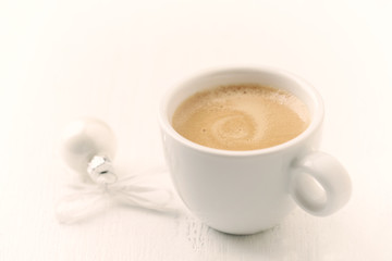 A cup of coffee and a small Christmas bauble and white wooden background. Close up. Copy space. 