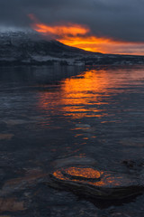 Beautiful orange sunset sunset landscape with pink clouds in a fjord reflection in Norway near the city of Tromso with hoarfrost on the rocks near the ocean