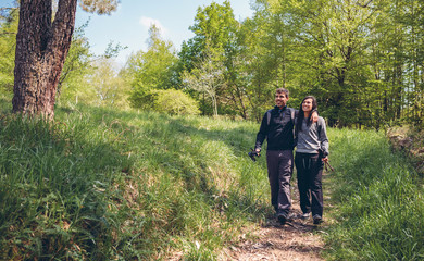 Couple of hikers walking embraced holding trekking sticks outdoors