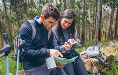 Young couple doing trekking sitting looking mobile and map outdoors