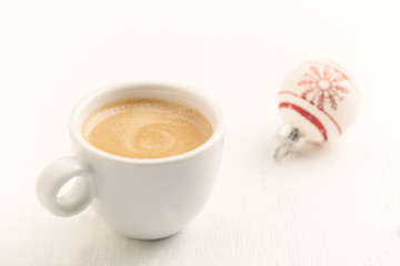 A cup of coffee and a small Christmas bauble and white wooden background. Close up. Copy space. 