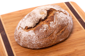 Loaf of organic farmer's bread with slices, isolated on a wooden cutting board.