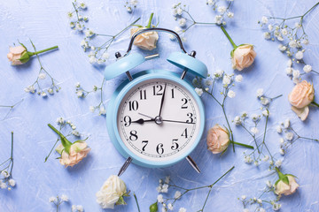 Blue alarm clock and pattern from fresh white gypsofila and rose  flowers on blue textured background.