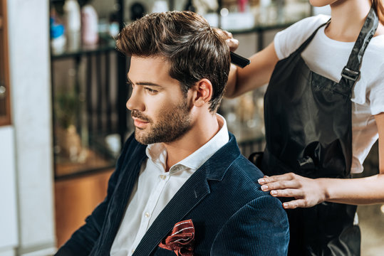 Cropped shot of hairstylist combing hair to handsome young man in beauty salon