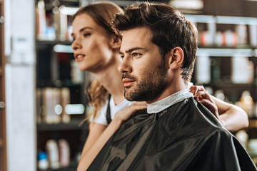 Handsome young man and beautiful female hairstylist looking away in beauty salon