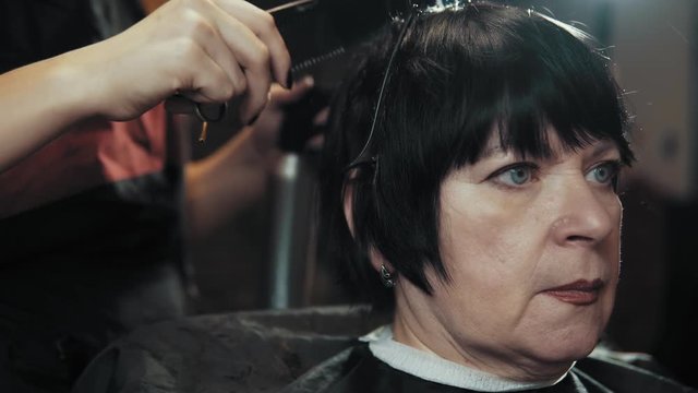 Mature Woman Having Her Hair Cut At The Hairdresser's. Closeup View Of A Hairdresser's Hands Cutting Hair With Scissors.