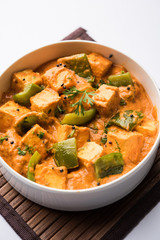 Malai or achari Paneer in a gravy made using red gravy and green capsicum. served in a bowl. selective focus