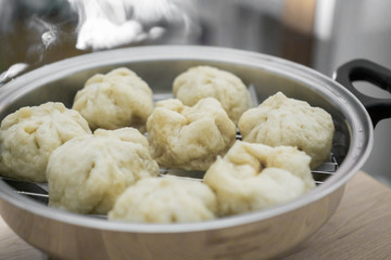 Fototapeta na wymiar Chinese dumplings (buns) being steamed on a modern stainless steel wok pan