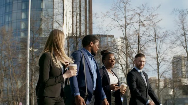 Pan shot of four multi-ethnic male and female colleagues walking and drinking coffee during coffee break