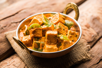 Malai or achari Paneer in a gravy made using red gravy and green capsicum. served in a bowl. selective focus