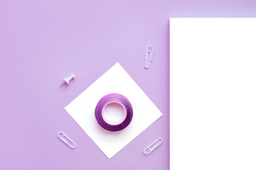 Beautiful office stationery flatlay with ruled notebook, pen, sticky note and paper clip on the bright desk with violet background.