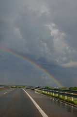 Empty highway during a storm with dramatic clouds and a beautiful rainbow. Driving on a rainy day. 