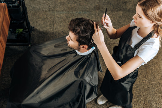 high angle view of hairstylist cutting hair to handsome young man in beauty salon