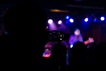 Fototapeta na wymiar Silhouette of hands using smart phone to take pictures and videos at live concert; Smartphone records live music; Take photo in front concert stage