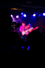 Silhouette of hands using smart phone to take pictures and videos at live concert; Smartphone records live music; Take photo in front concert stage